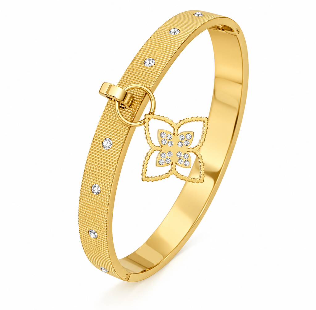 Gold textured hinged bangle bracelet featuring inset crystal accents and a dangling pave floral clover charm on a plain white background.
