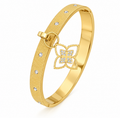 Gold textured hinged bangle bracelet featuring inset crystal accents and a dangling pave floral clover charm on a plain white background.
