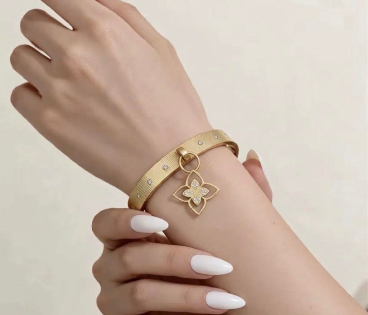 Gold textured charm bangle bracelet with cz accents and dangling pave clover on model wrist.
