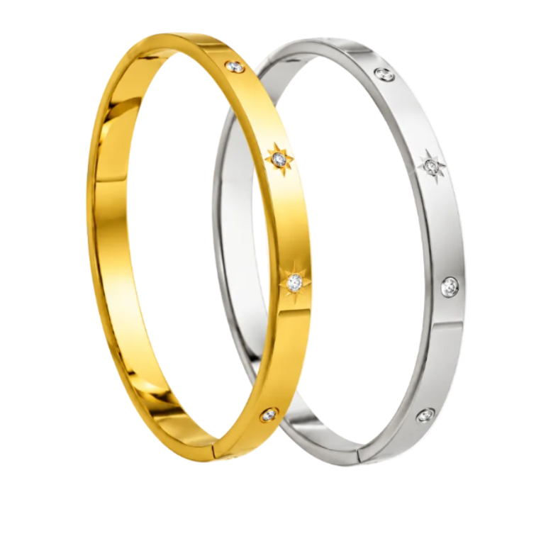 Two sleek oval bangle bracelets—one polished gold and one silver—adorned with clear inset stones, some featuring starburst engravings around the gems.