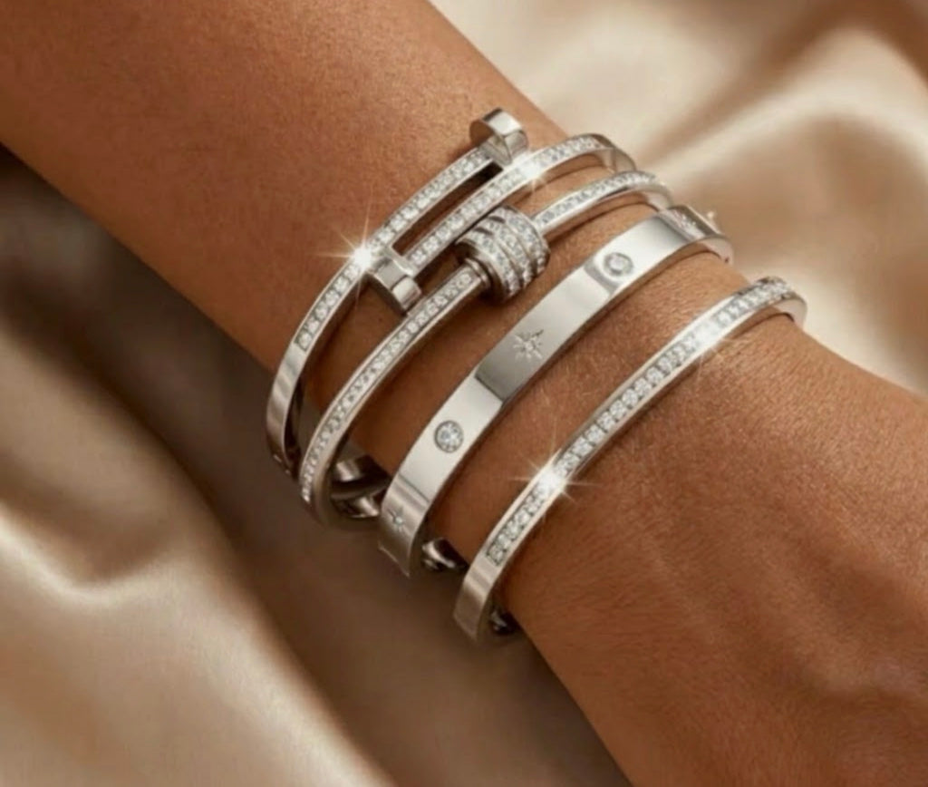 Stack of silver pave diamond cuff bangles and star-engraved wrist bracelets on model against cream satin.