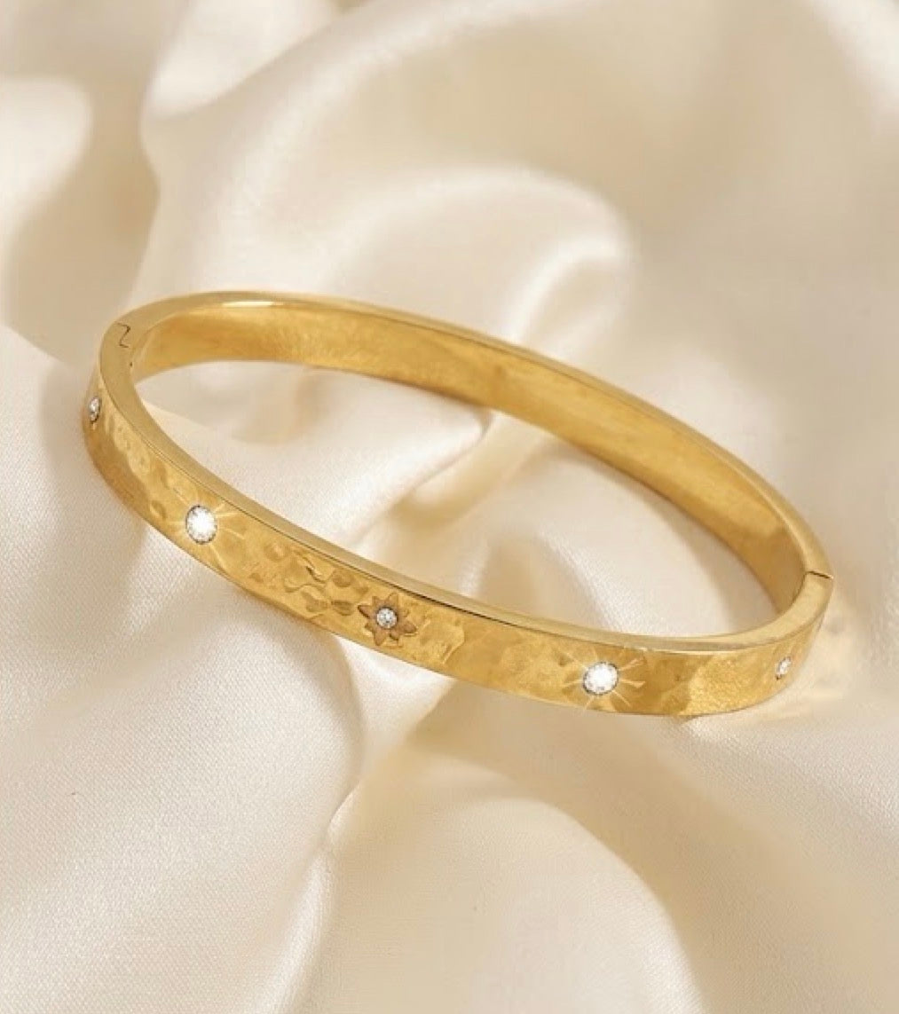 Gold smooth starburst cz bangle bracelet engraved celestial cuff on ivory satin background.