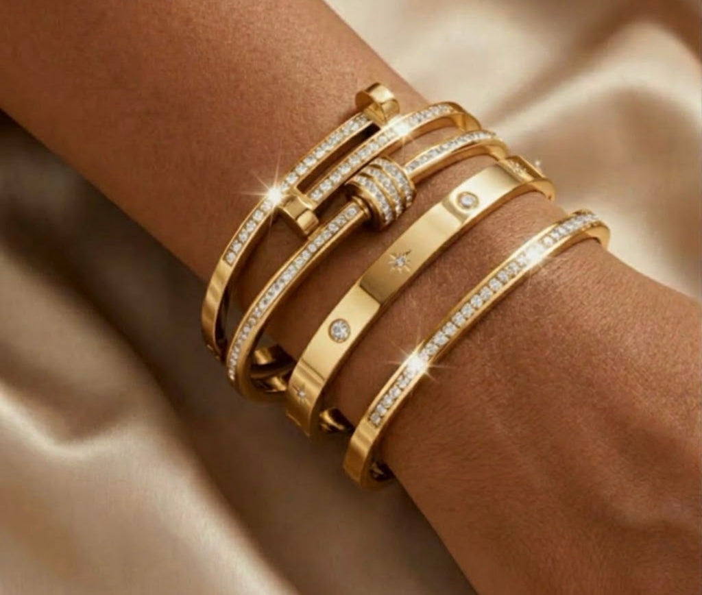 Stack of four gold diamond-accented bangles including nail-motif and star-engraved cuff bracelets on a wrist.