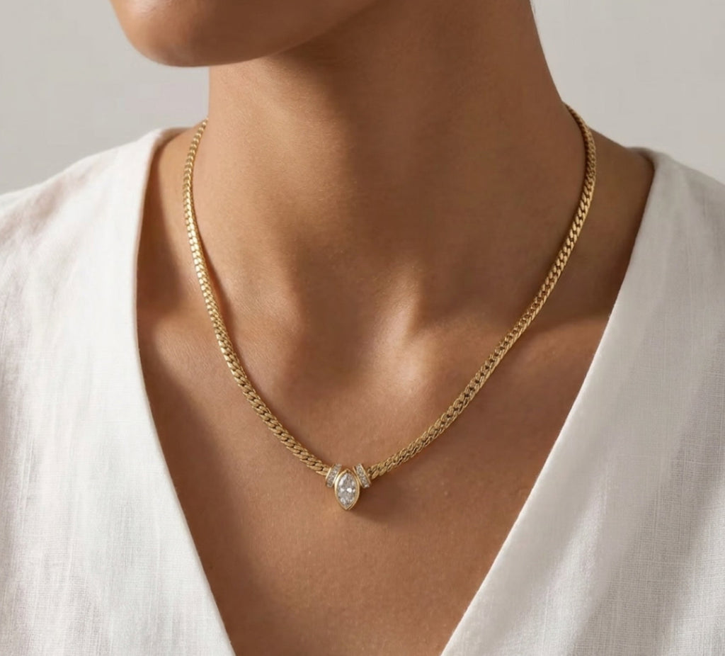 A model wearing a gold curb-style chain necklace with a central marquise-cut diamond pendant against a white shirt.