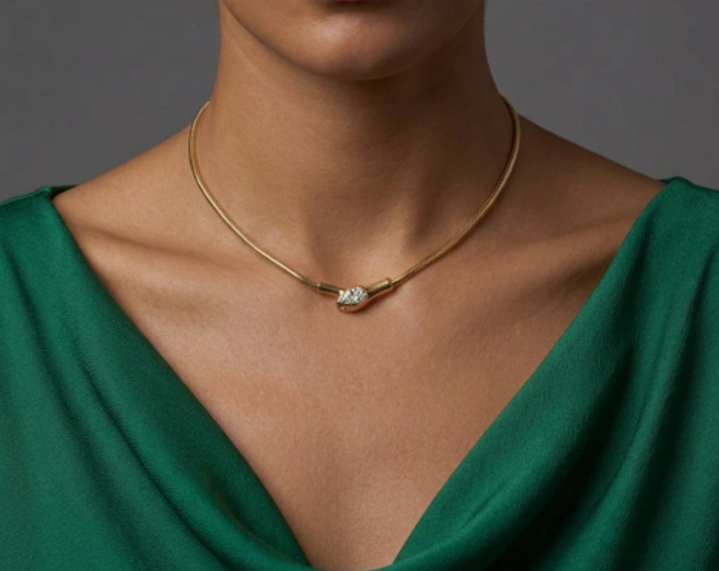 A woman wearing a gold rigid collar necklace with a pave-set diamond serpent head centerpiece, styled with an emerald green cowl-neck top.