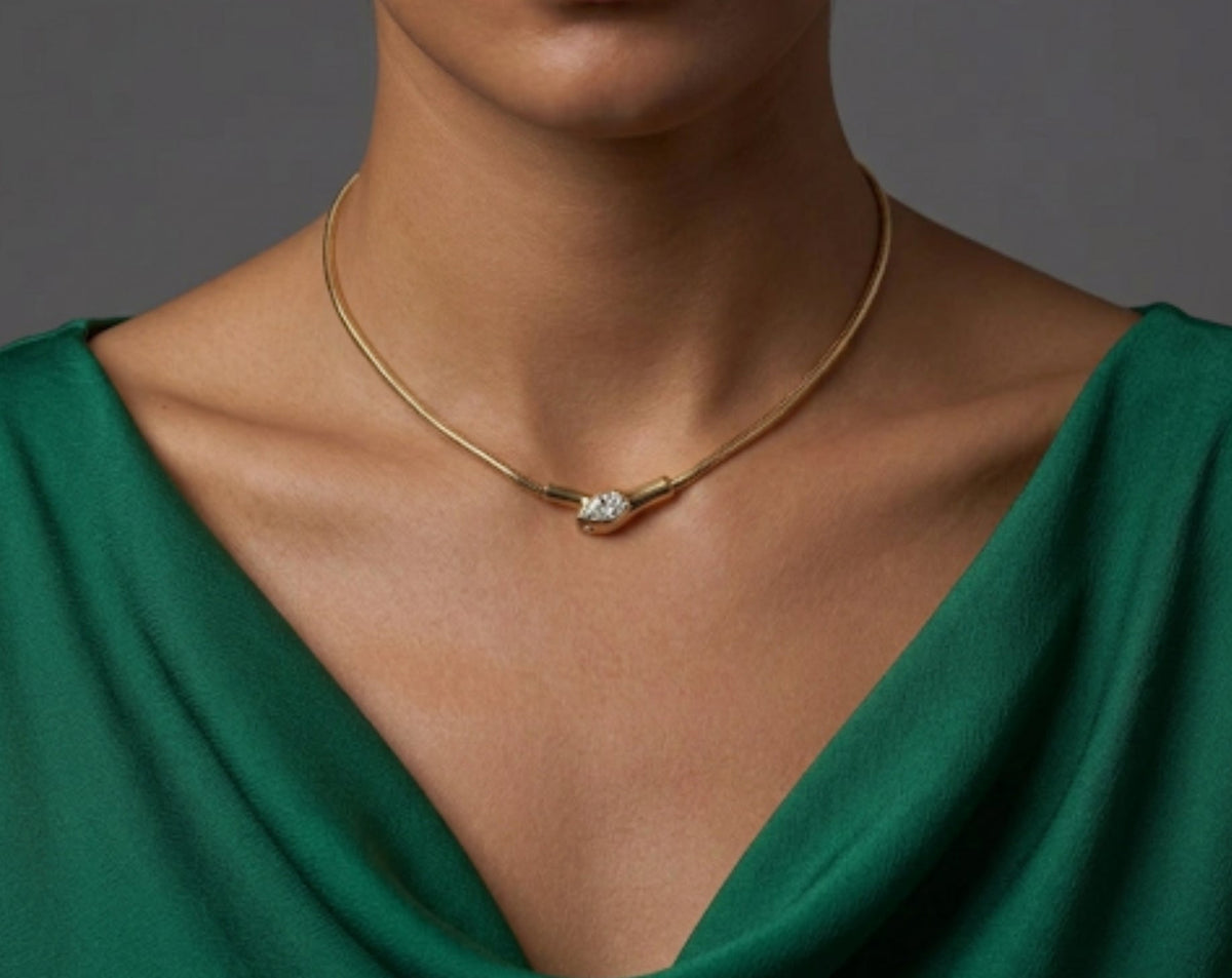 A woman wearing a gold rigid collar necklace with a pave-set diamond serpent head centerpiece, styled with an emerald green cowl-neck top.
