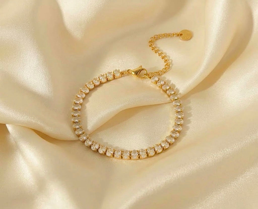 Gold cz tennis bracelet adjustable crystal chain jewelry on white satin background.