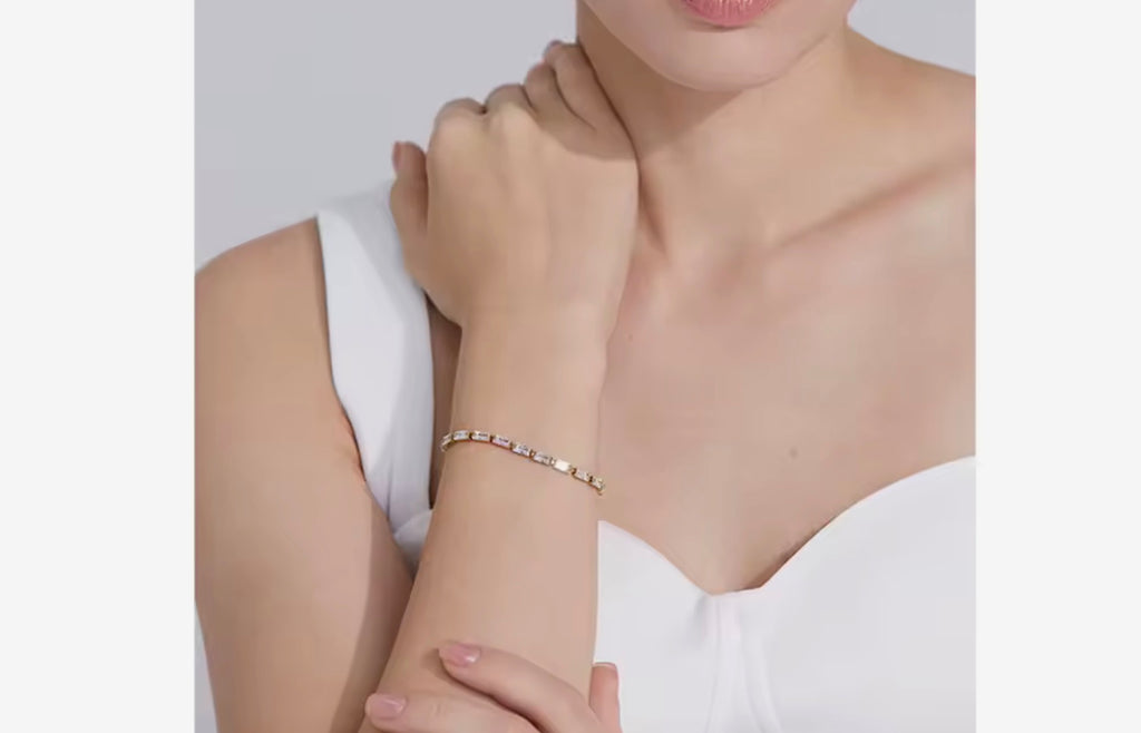 Woman wearing a delicate gold baguette cubic zirconia tennis bracelet on her wrist with a white top.