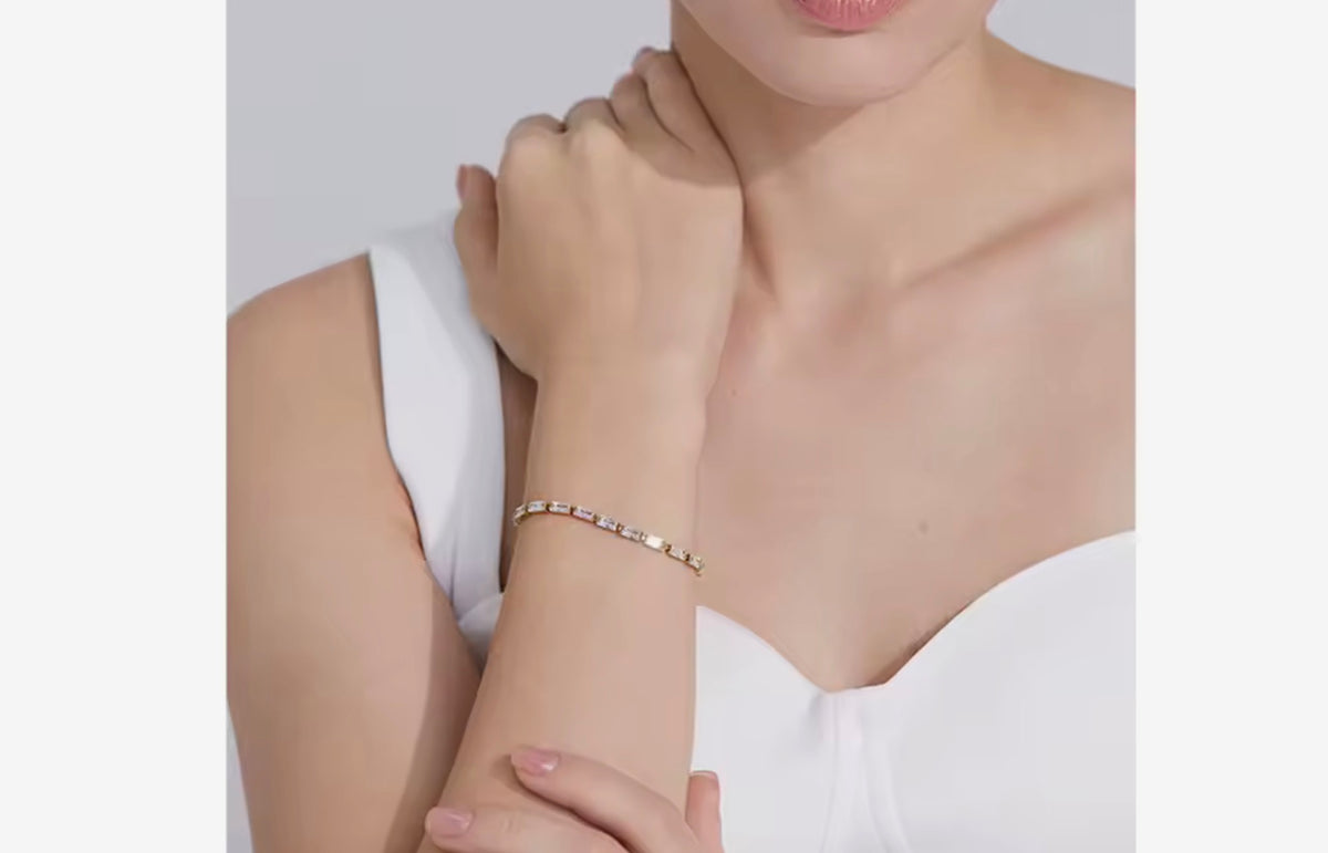 Woman wearing a delicate gold baguette cubic zirconia tennis bracelet on her wrist with a white top.