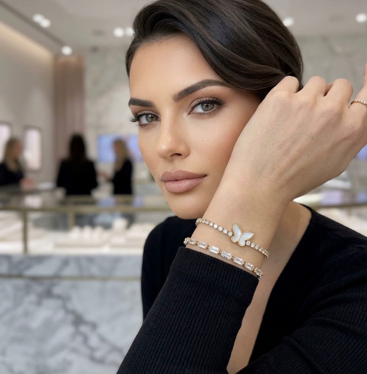 Woman wearing a stacked gold mother-of-pearl butterfly charm tennis bracelet alongside a gold baguette CZ bracelet.